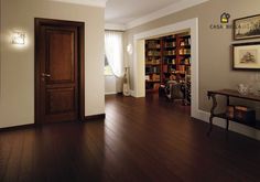 an empty room with wooden floors and bookshelves on the wall, in front of a door that leads to another room