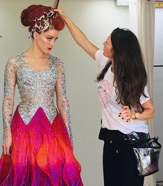 two women standing next to each other in front of a white wall and one wearing a colorful dress