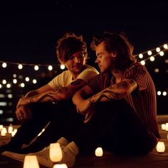 two young men sitting on the ground in front of some lit candles and looking at each other