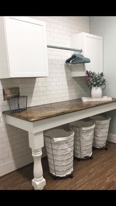 a kitchen with white cabinets and wooden counter top next to three trash cans on the floor