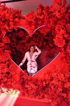 a woman standing in front of a giant heart surrounded by red flowers and fake roses