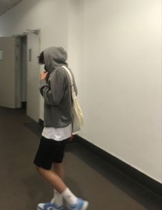 a man walking down a hallway talking on a cell phone and wearing a hoodie