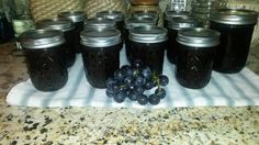 grapes and jam are sitting on a towel in front of mason jars with black lids