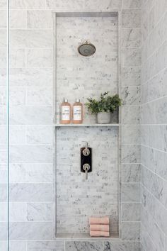 a white tiled shower with shelves and plants on the wall, along with toiletries