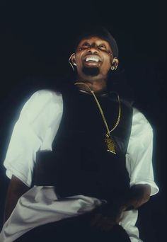 a man in black vest and white shirt with gold chains on his neck, laughing