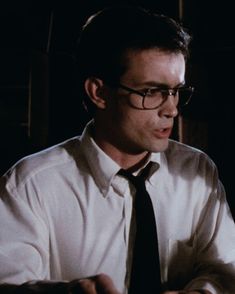 a man wearing glasses and a tie is looking at his cell phone in the dark