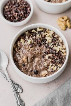 three bowls filled with oatmeal and nuts on top of a white table