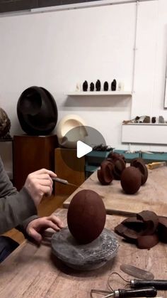 a woman is working with clay on a wooden table in front of other pottery items