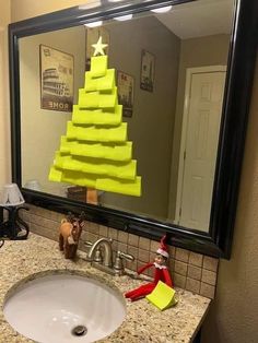 a christmas tree made out of yellow sticky notes is reflected in the bathroom sink mirror