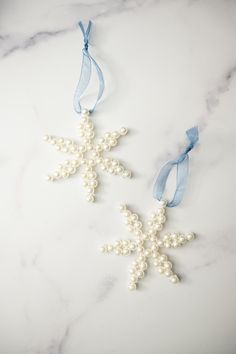 two snowflake ornaments on a marble countertop with blue ribbons and pearls hanging from them