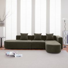 a green couch sitting on top of a white rug in a living room next to windows