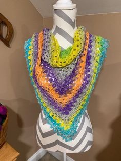 a multicolored crocheted shawl is on display in a room next to a mannequin