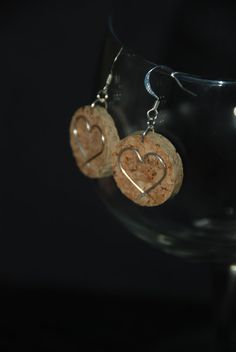 wine cork earrings with two hearts hanging from them in front of a wine glass on a black background