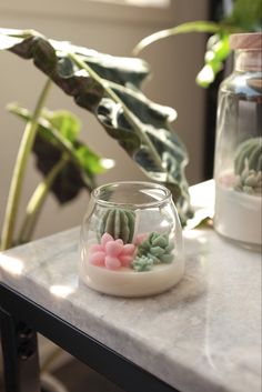 a small glass bowl filled with flowers on top of a table next to a potted plant