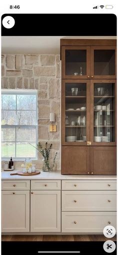 a kitchen with white cabinets and stone walls, along with an open window to the outside