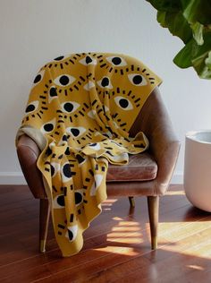 a chair with a yellow and black blanket on top of it next to a potted plant