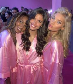 three beautiful young women standing next to each other in front of a group of people