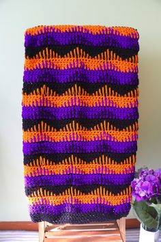 a purple and orange crocheted blanket sitting on top of a wooden chair next to a potted plant