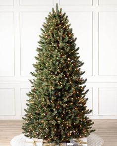 a small christmas tree with lights and presents on the floor in front of a white wall