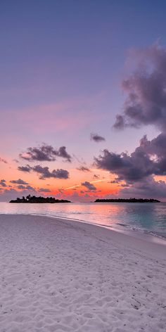 the sun is setting on an empty beach with footprints in the white sand and blue water