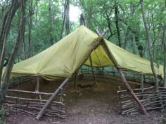 a yellow tent in the woods surrounded by bamboo poles and trees with no leaves on it