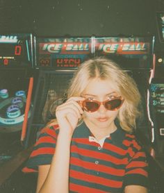 a woman wearing sunglasses standing in front of a slot machine with her hand on her face