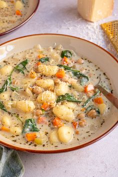 two bowls filled with soup on top of a white table next to cheese and bread