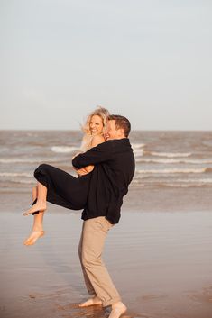 a man carrying a woman on his back at the beach while she holds him in her arms