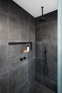 a bathroom with gray walls and black fixtures, including a shower head in the corner