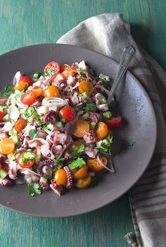 a salad with octopus and tomatoes in a bowl on a green tablecloth next to a fork