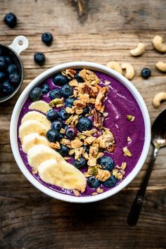 a bowl filled with blueberries, bananas and granola on top of a wooden table