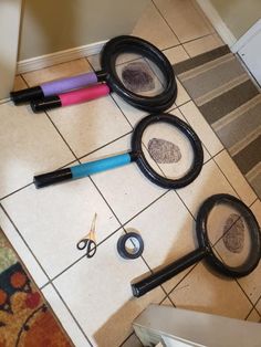 three magnifying glasses with fingerprints and scissors on the floor next to each other