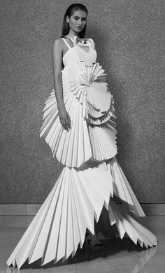 a black and white photo of a woman wearing a dress made out of folded paper