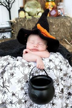 a sleeping baby wearing a witches hat and holding a caulder in it's lap