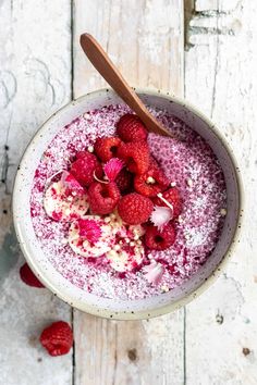 a bowl filled with raspberries on top of a white wooden table next to a spoon