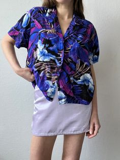 Purple & blue multi-color printed short sleeve collared tee by Jams World with purple buttons down the front. Unlined with a boxy fit. In excellent vintage condition. DETAILSLabel: Jam's WorldMade in USAMaterial: 100% Rayon SIZE & MEASUREMENTSTag Size: Large Best Fits: XS/Small Length: 22" Bust: 44"Waist: 44"Sleeve: 8"Shoulder: 18" Purple Printed Shirt With Short Sleeves, Purple Collared Top With Graphic Print, Purple Floral Print Short Sleeve Shirt, Retro Purple Short Sleeve Top, Purple Floral Print Short Sleeve Tops, Retro Short Sleeve Purple Shirt, Retro Purple Short Sleeve Shirt, 90s Style Purple Short Sleeve Tops, Purple Short Sleeve 90s Tops