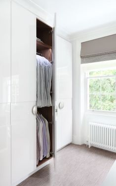 an open closet with clothes hanging on the doors and drawers in front of a window