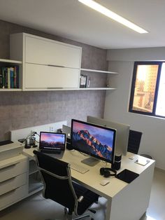 two computer monitors sitting on top of a desk in front of a book shelf filled with books