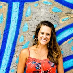 a woman standing in front of a wall with graffiti on it and smiling at the camera