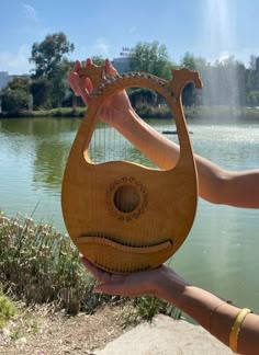 a person holding a wooden instrument in front of a body of water with trees and buildings in the background