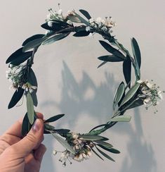 a hand holding a flower crown with white flowers and green leaves