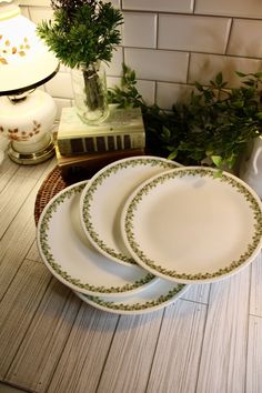 three white plates sitting on top of a table next to a vase with green leaves