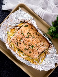 a piece of salmon on foil with vegetables and parsley next to it sitting on a tray