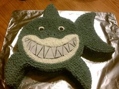 a cake shaped like a shark on top of aluminum foil covered in icing and decorated with white teeth