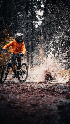 a man riding a bike through a forest filled with trees and water splashing on the ground