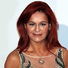 a woman with red hair wearing a green and gold dress smiling at the camera while standing in front of a white wall