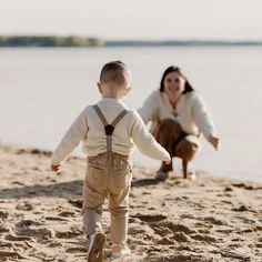 a woman kneeling down next to a little boy on top of a sand covered beach