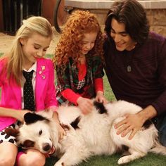 two girls and a man petting a dog on the grass