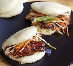 two buns filled with meat and vegetables sitting on a black plate next to another bun