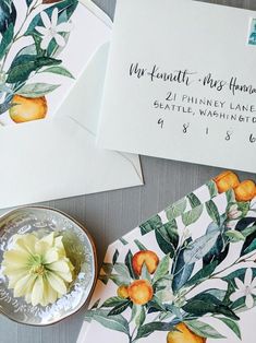 two envelopes with oranges and leaves on them next to a bowl of flowers